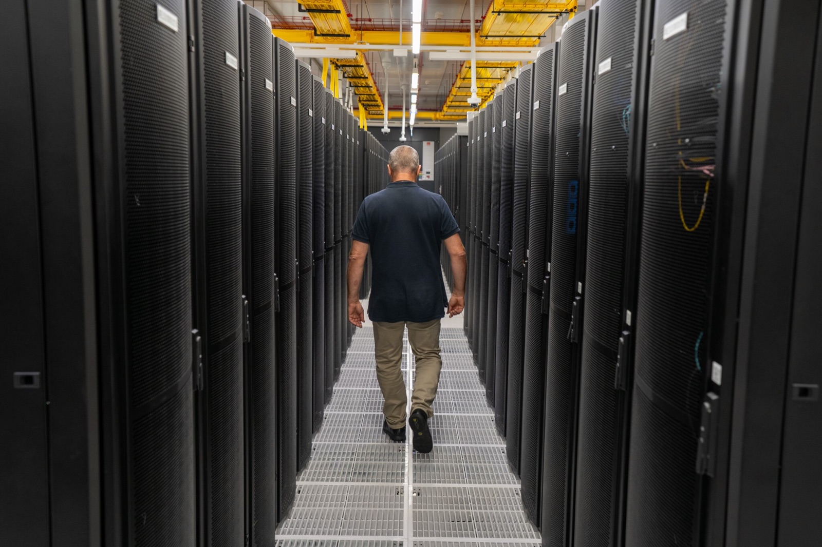 A technician walks between rows of server racks inside a large data centre.